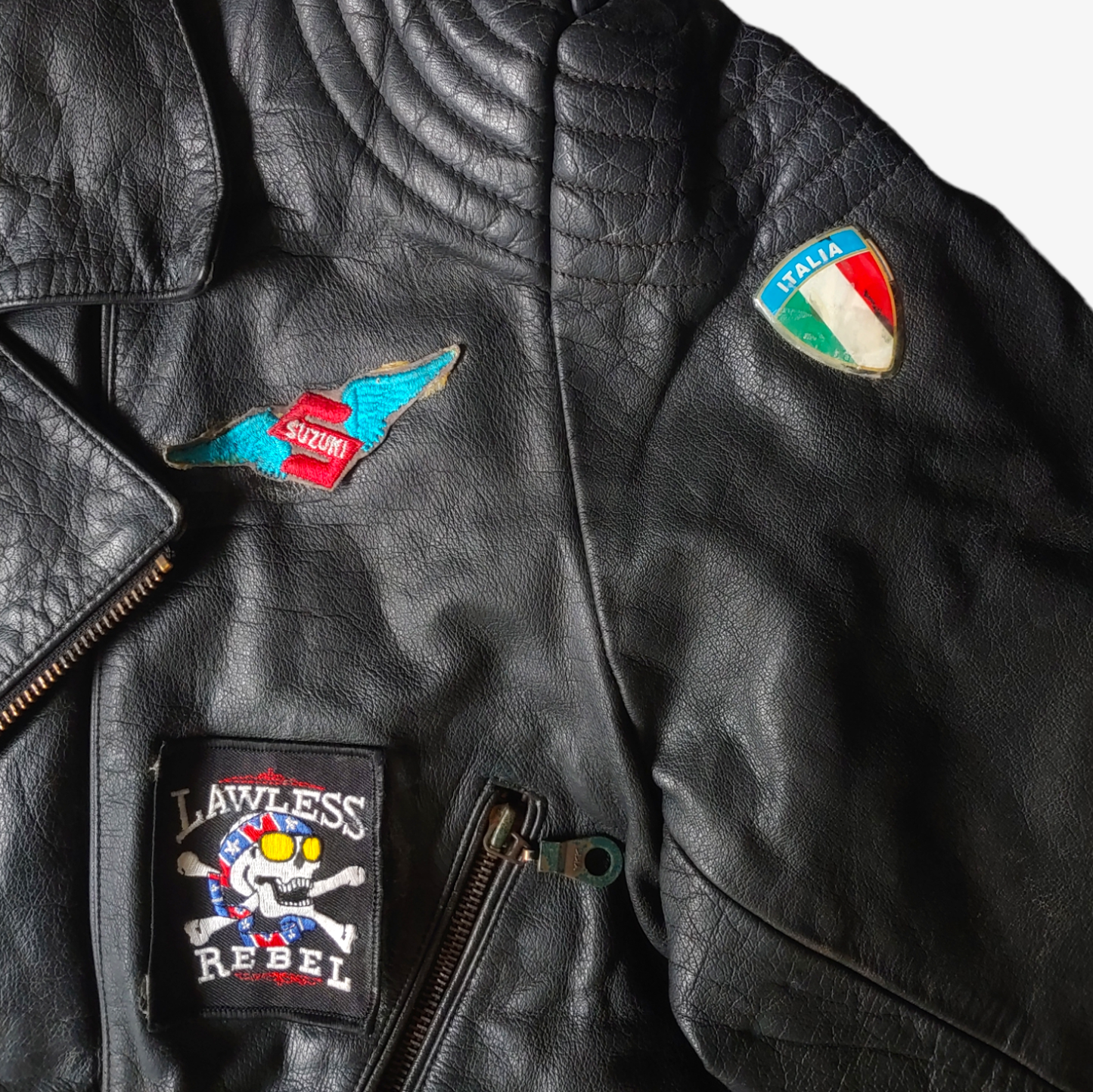 Embroidered badges on a black leather biker jacket with a skull and aces design on its back.