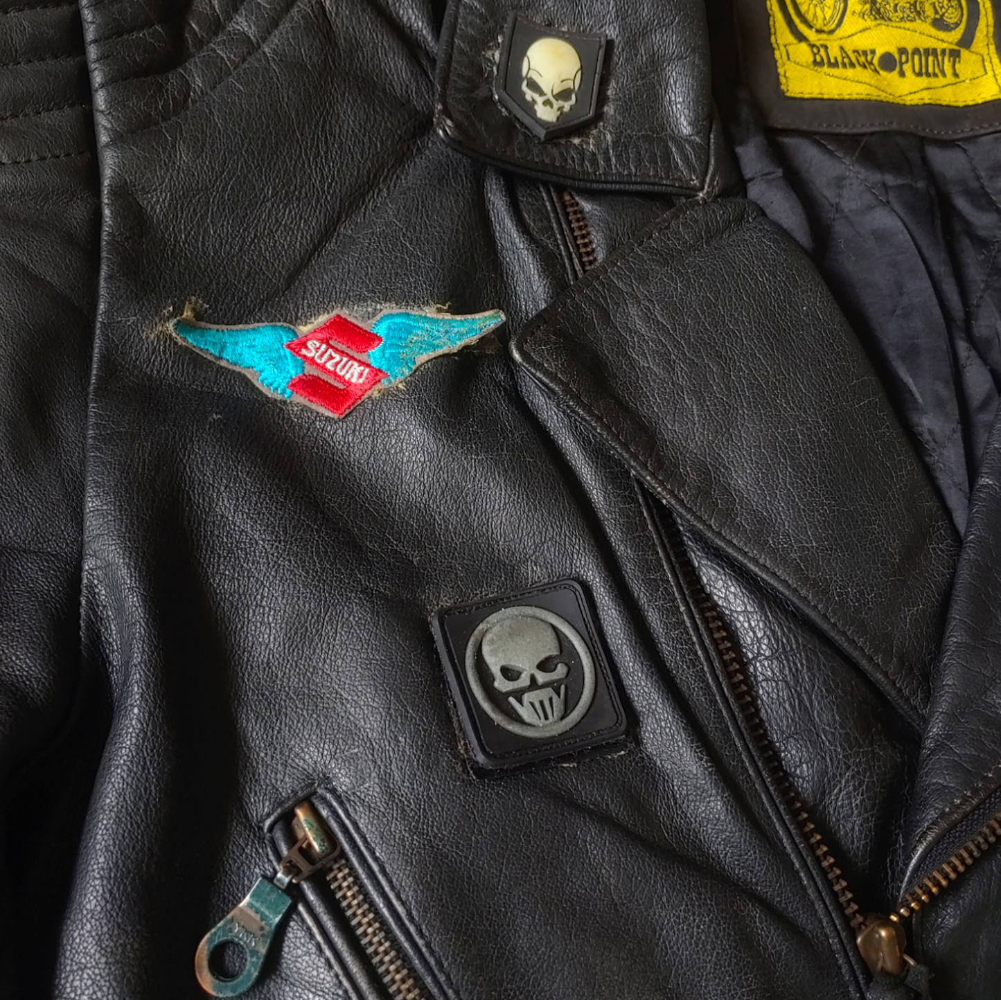 Embroidered crests on black leather biker jacket with a skull and aces design on the back.