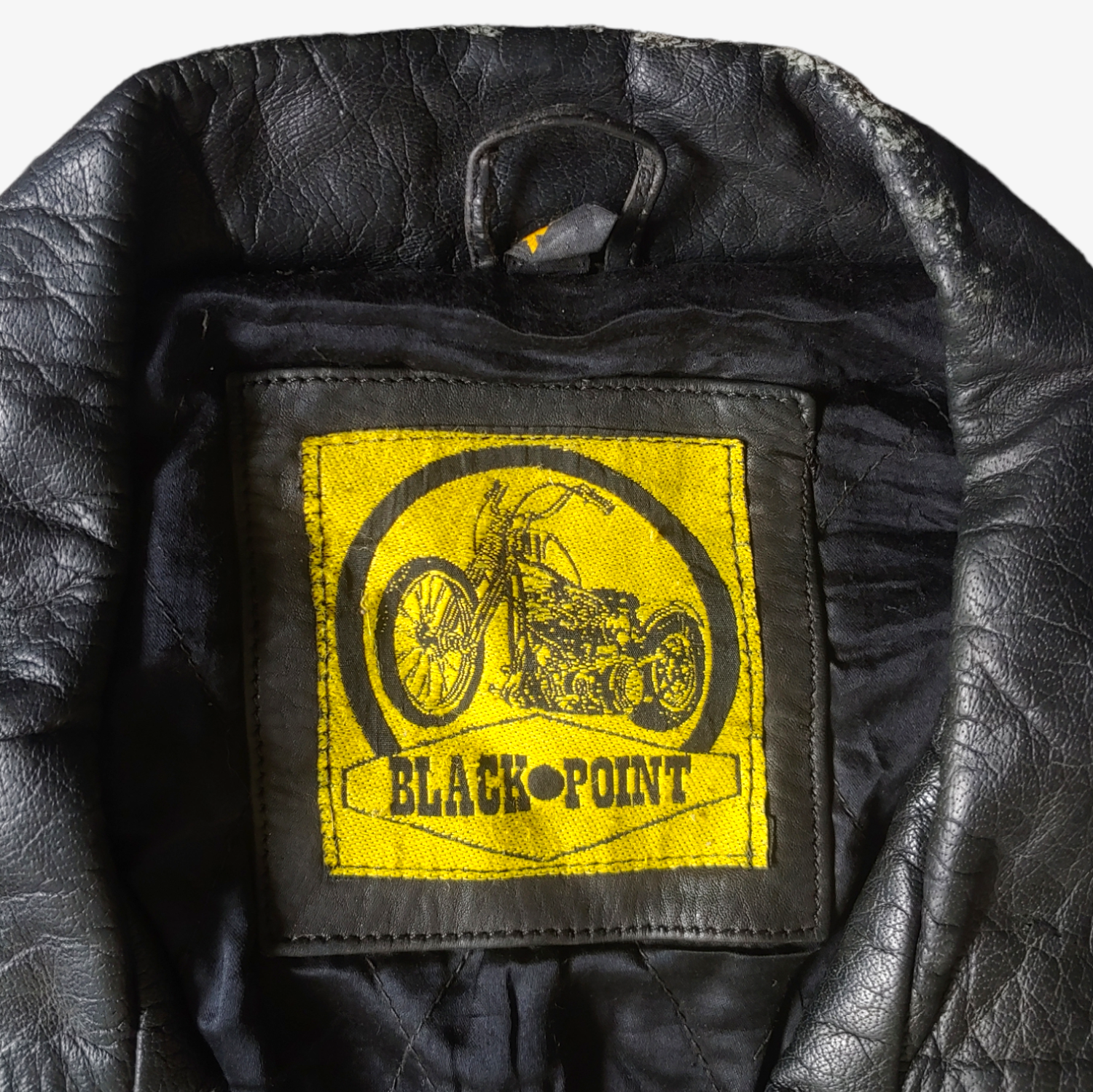 Label of black leather biker jacket with a skull and aces design on the back, featuring multiple zipped pockets and a belted waist.