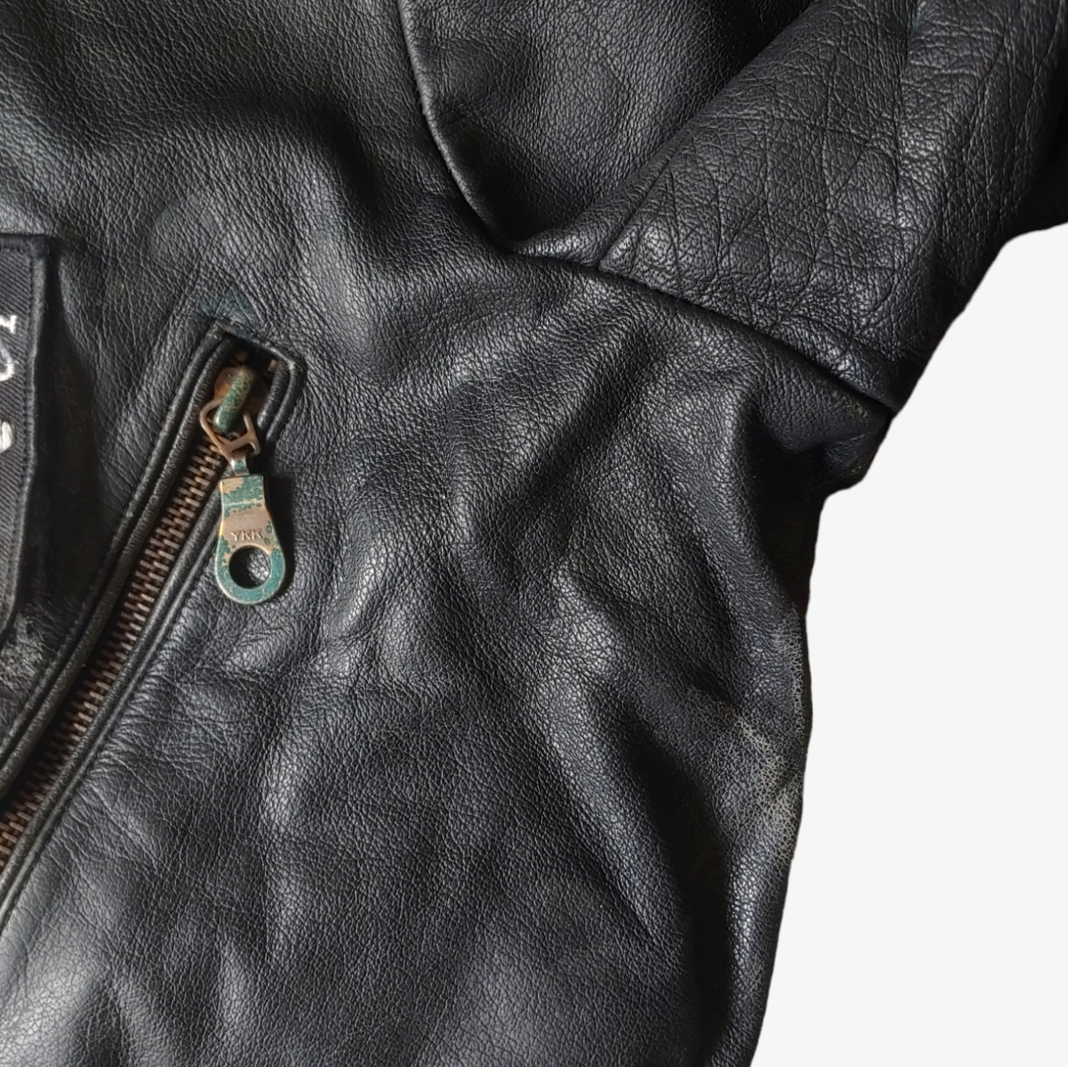 Wear of zipper on black leather biker jacket with a skull and aces design on the back.