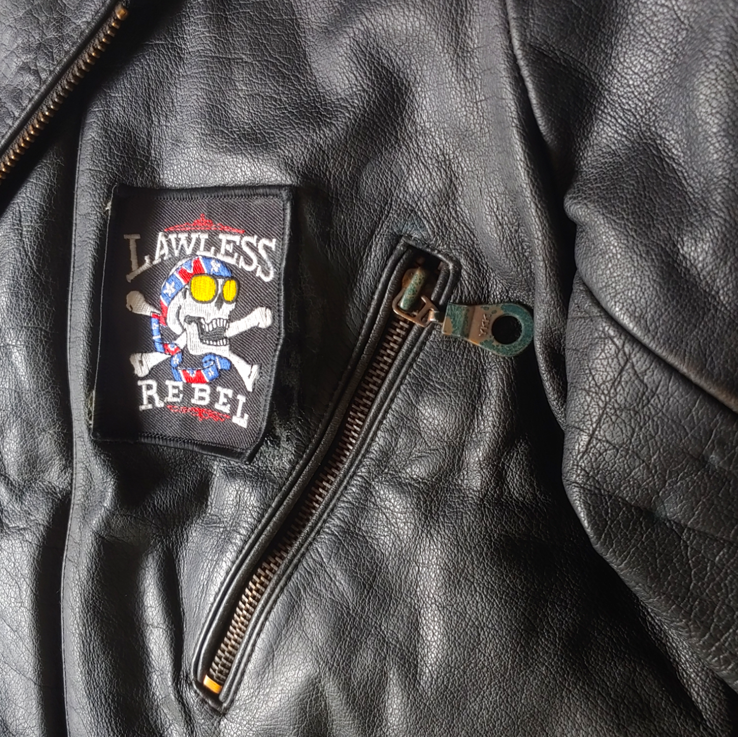 Patina zipper of black leather biker jacket with a skull and aces design on the back.