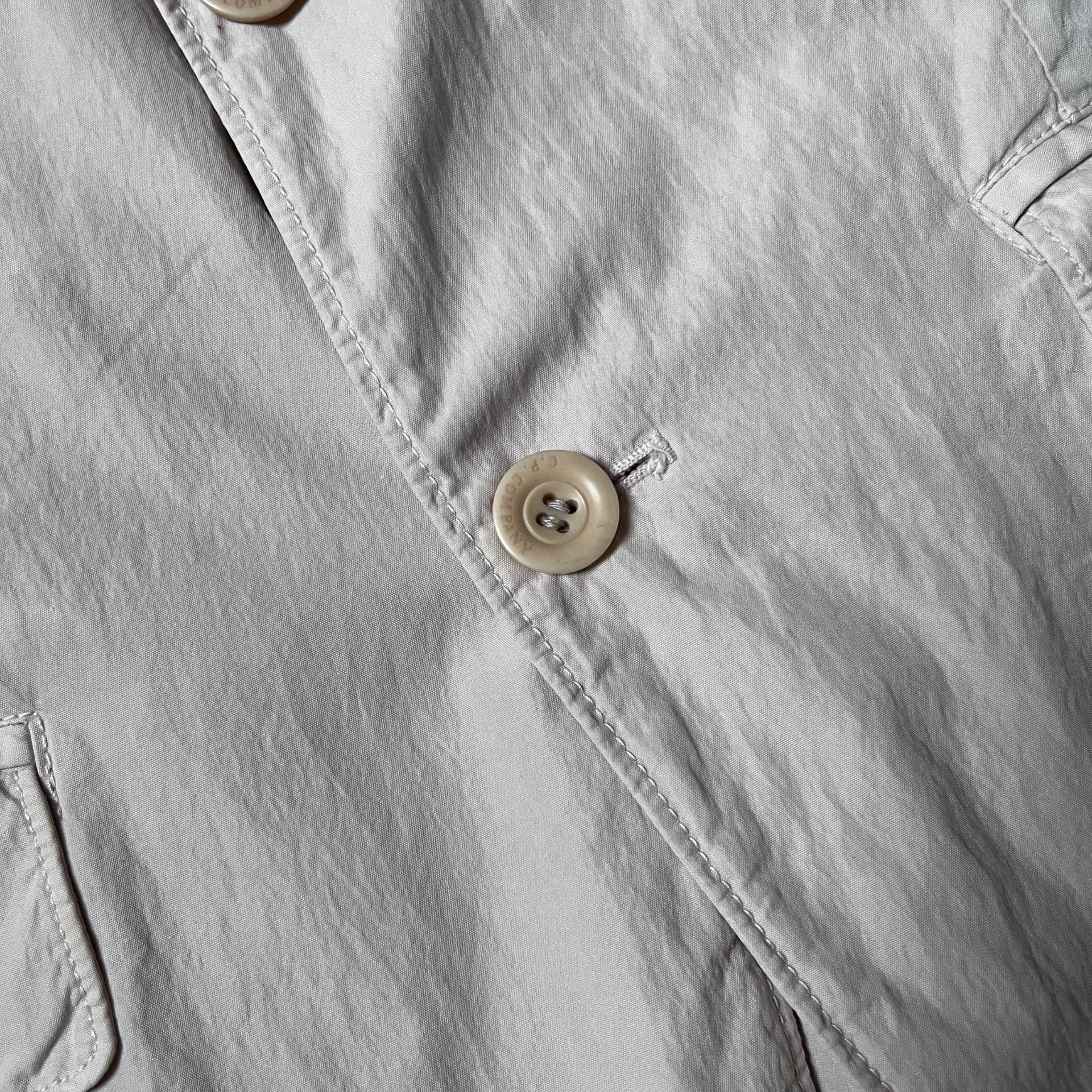 Close up of a CP Company engraved button of a vintage Y2K men's cream single breasted blazer.