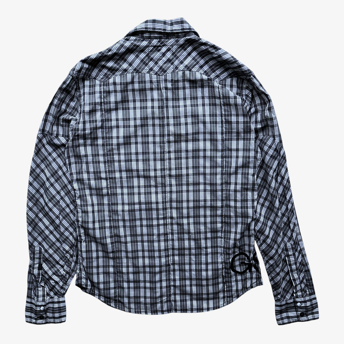A long-sleeve G-Star plaid button-up shirt shown from the back, featuring a black, white, and grey checkered pattern with a small circular logo on the lower right back, set against a plain light grey background.