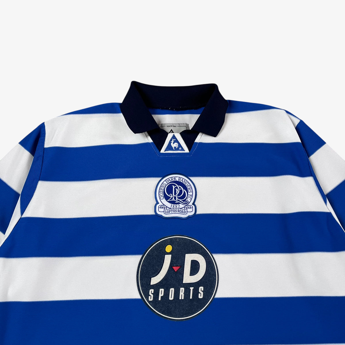 Close up of a vintage QPR 2001 blue and white striped sports jersey crest on a white background
