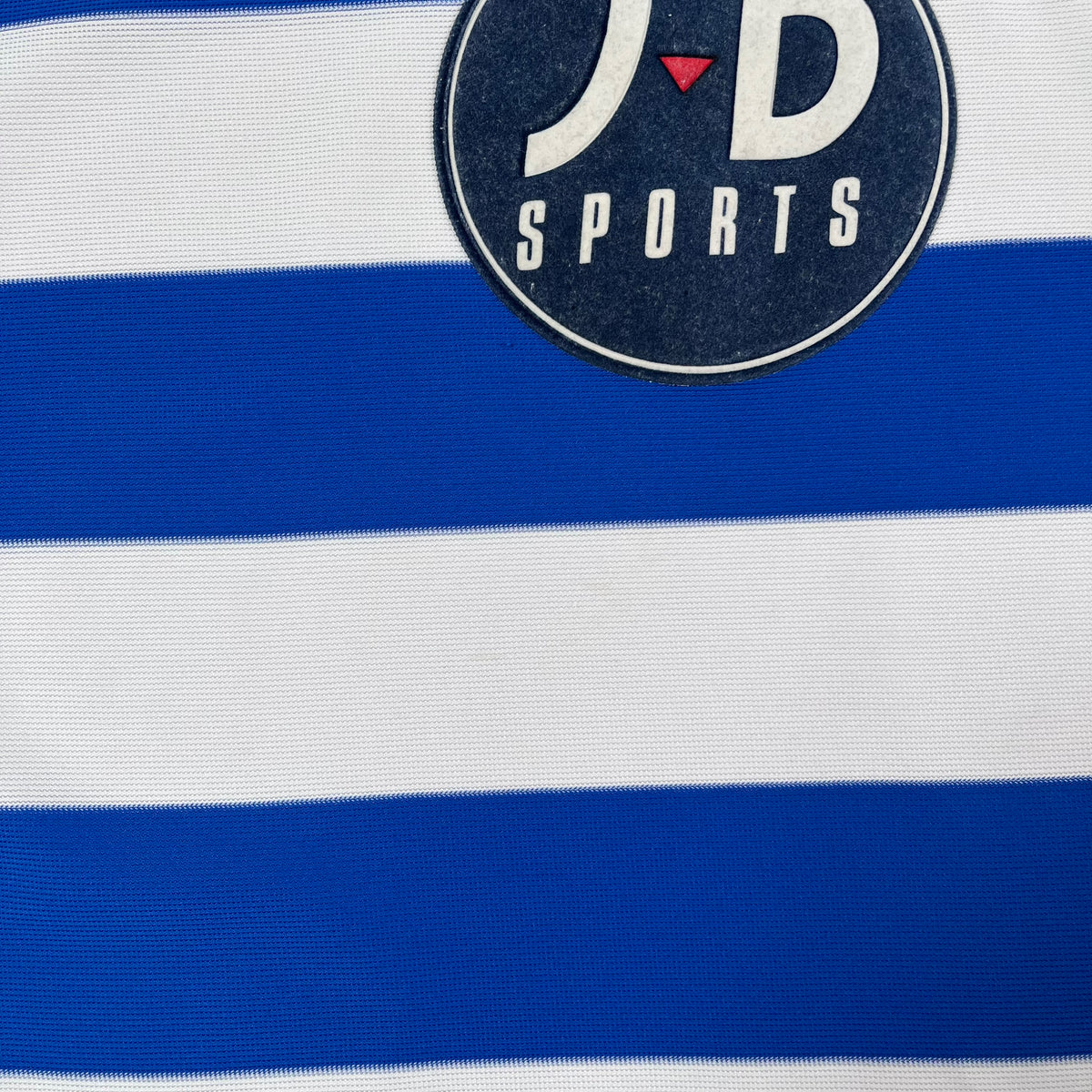Close-up wear of a vintage QPR blue and white striped jersey with a 'JD Sports' logo.