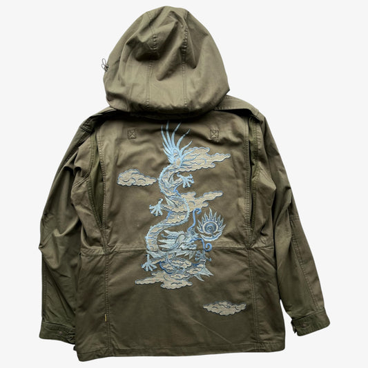 A khaki green Maharishi hooded jacket shown from the back, featuring a large light blue embroidered dragon design with clouds across the centre back.
