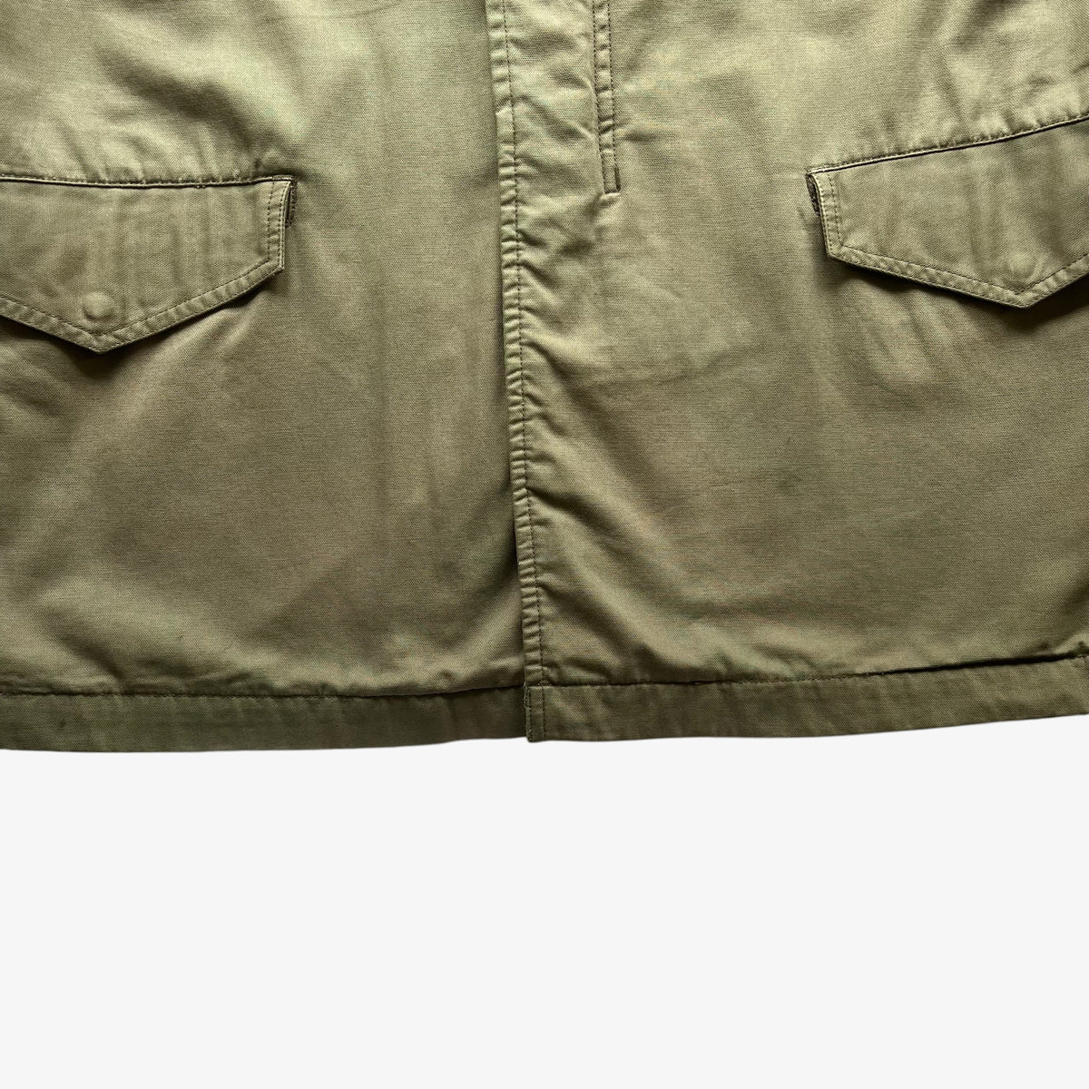 Close-up of olive green fabric with two angled flap pockets and a central seam, shown against a plain white background.