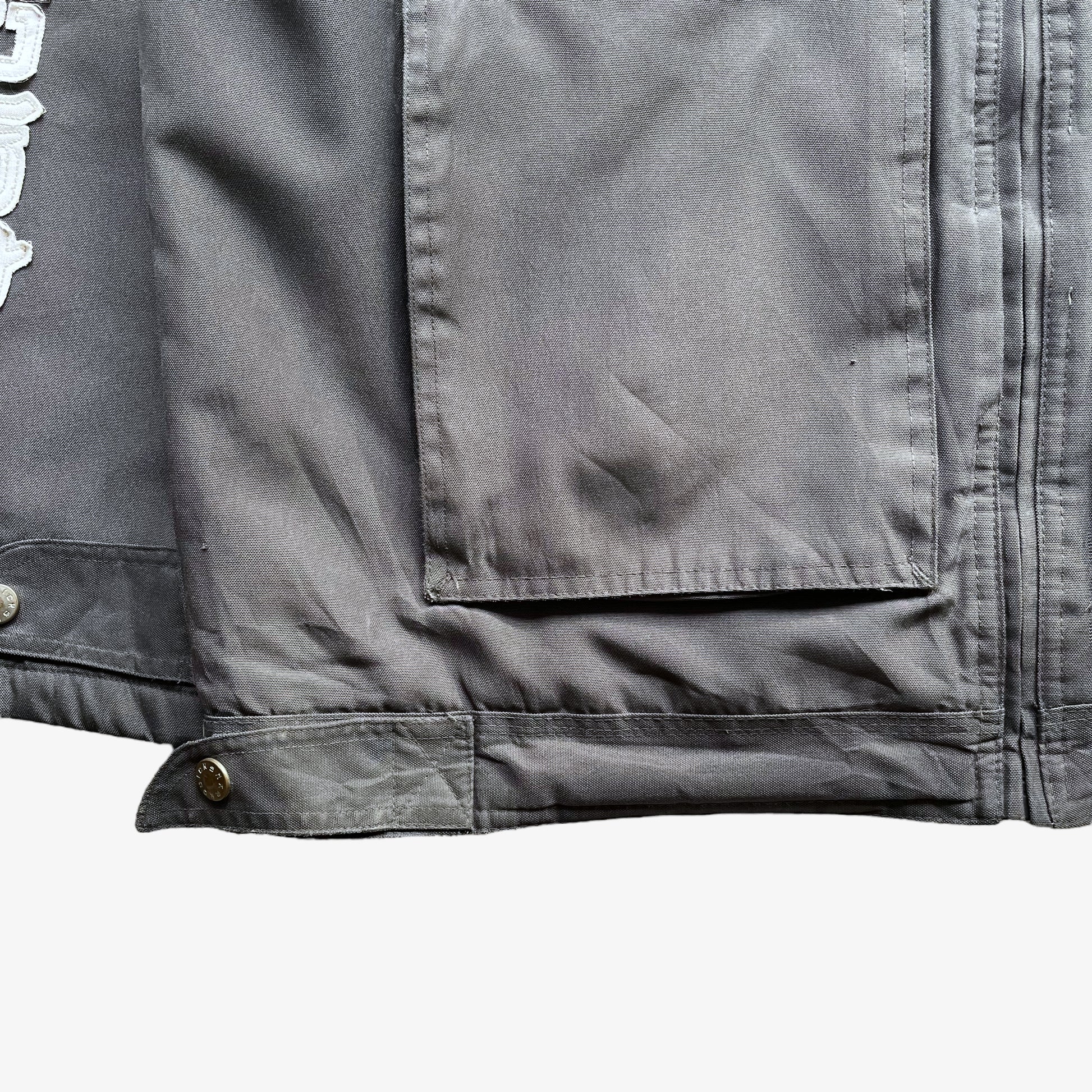 Cargo pockets of men's vintage Y2K Quickshark special aircraft supply grey utility jacket with back spell out.