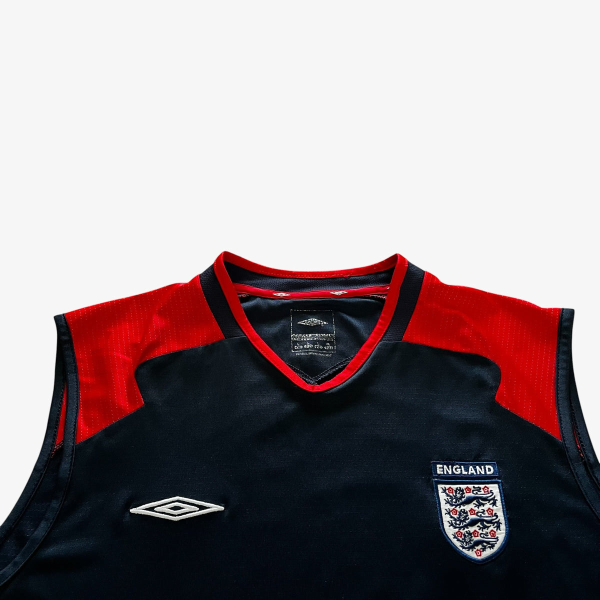 Close-up of a sleeveless England football jersey with a dark navy body, red shoulder panels, and the Umbro logo on the chest.