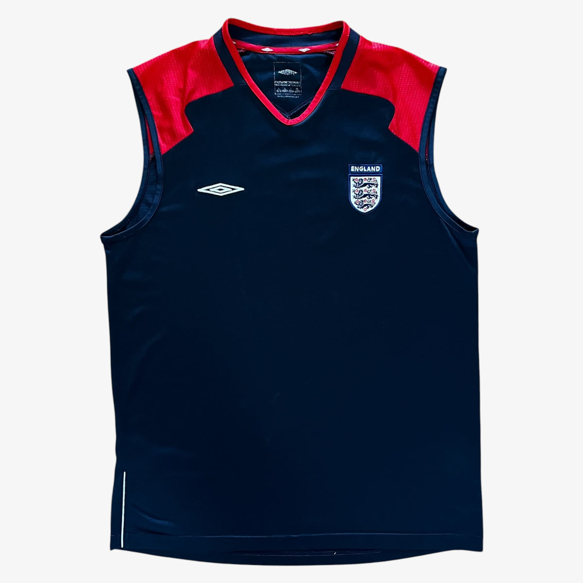A sleeveless navy blue athletic vest with red shoulder panels, featuring the Umbro logo on the right chest and the England national team crest on the left chest, displayed against a light gray background.