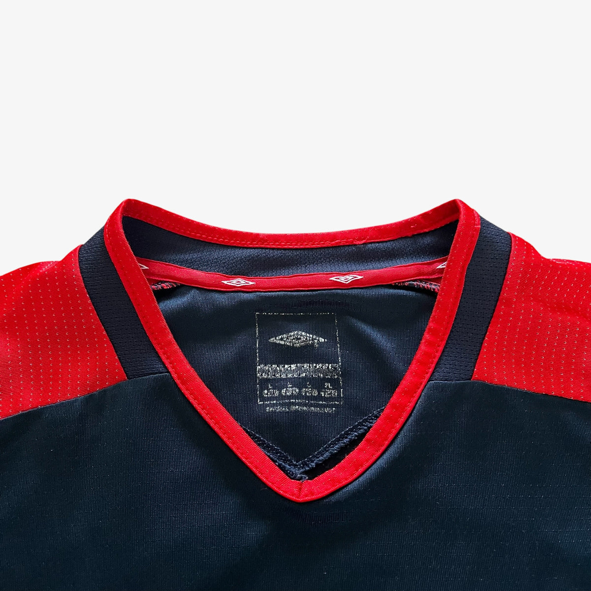 Close-up of a V-neck sports jersey showing the collar, with a navy blue body, red trim, and a visible diamond logo patch on the inner neck label.