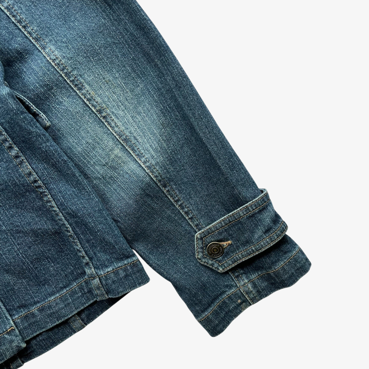 Close-up of a vintage women's Burberry blue denim jacket sleeve showing the buttoned cuff and pocket stitching on a light grey background.