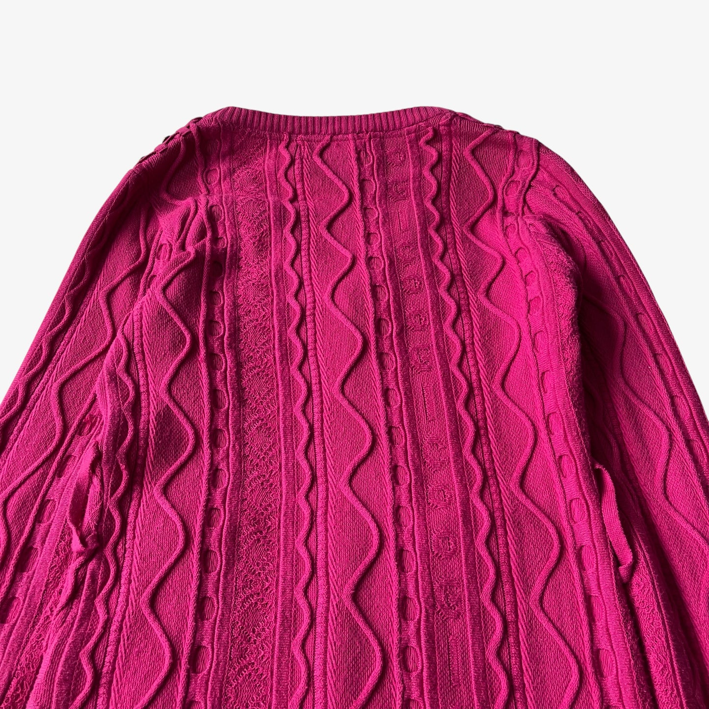 Close up of a vintage Coogi pink cable knit sweater on a white background.