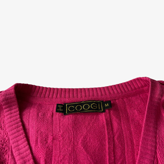 Close up of a pink sweater with a vintage COOGI label on a white background.