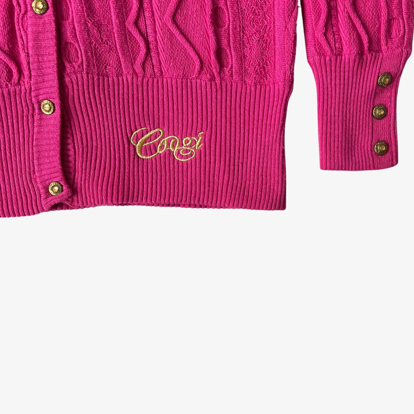 Close up of a pink cardigan with gold buttons and Coogi embroidered branding on a white background.
