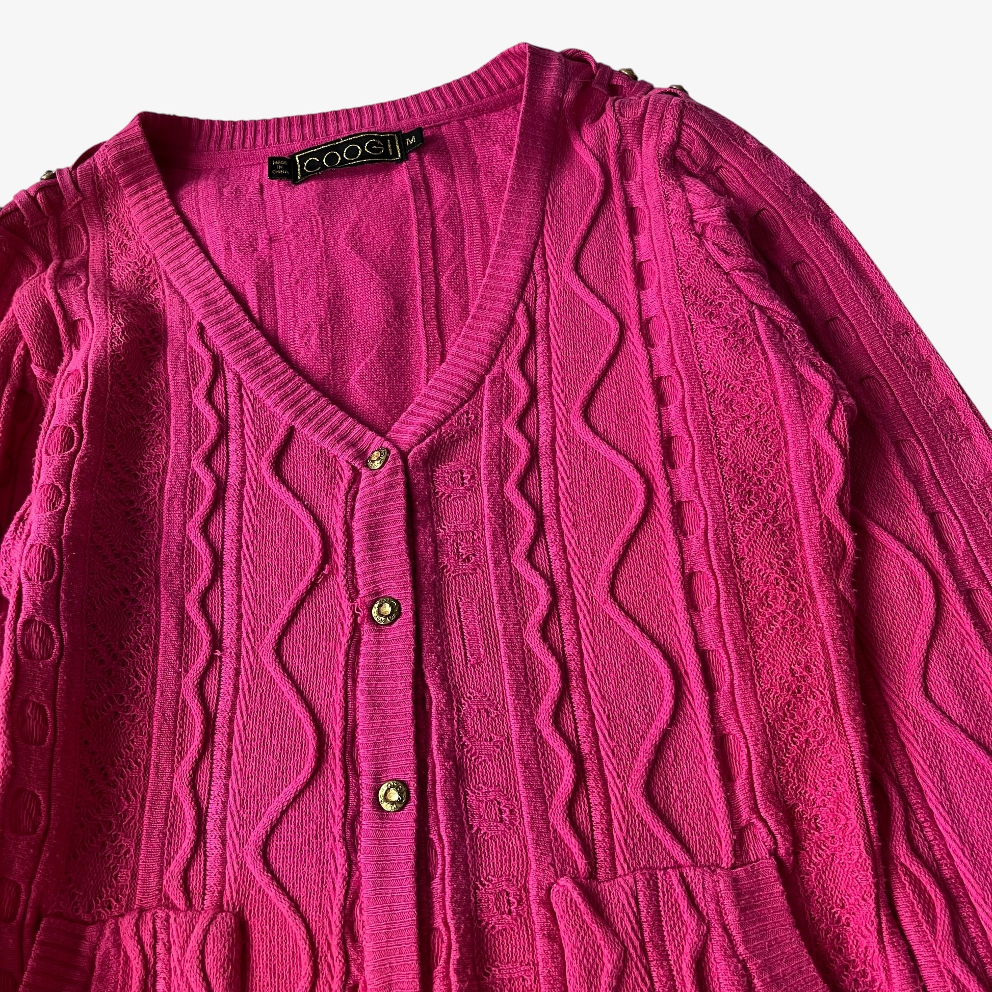 Vintage Coogi pink cardigan with cable knit pattern and button details on a white background.