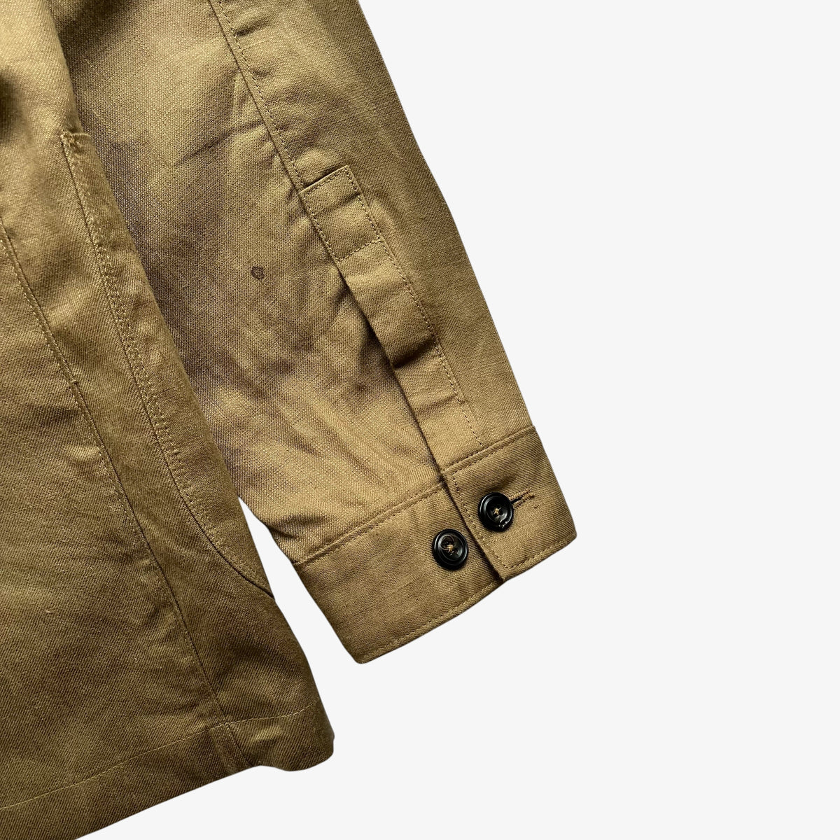 Close-up detail of a brown women's blazer sleeve showing a buttoned cuff and pocket seam on a light grey background.
