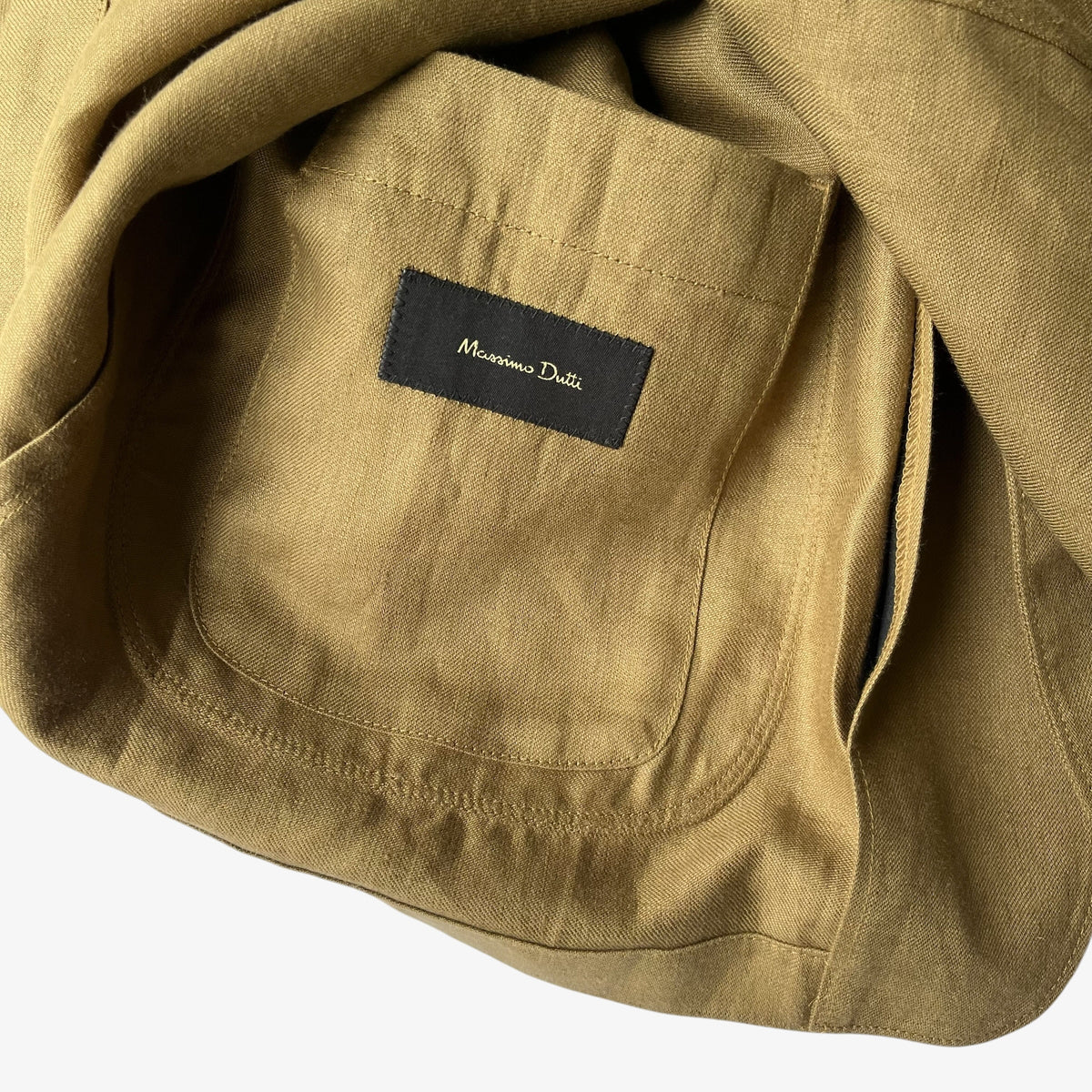 Close-up of a brown women's blazer showing a pocket with a black brand label that reads 'Massimo Dutti'.
