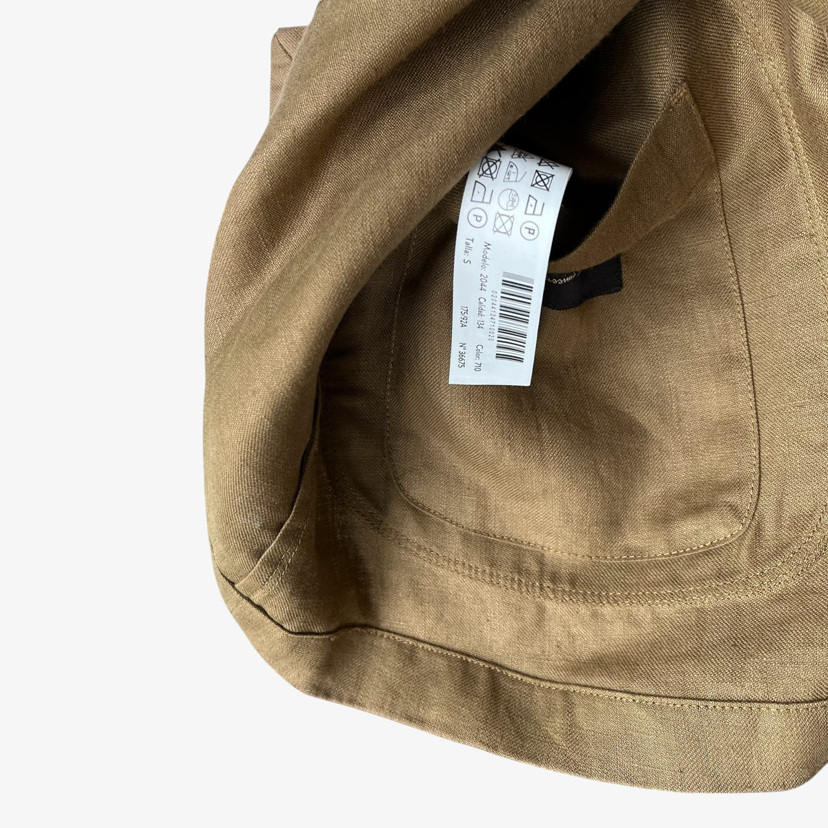 Close-up of a women's brown blazer showing the interior lining, stitched pocket edge, and a white care label with a barcode against a light grey background.