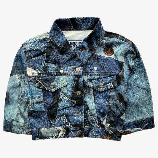 A women's Moschino denim jacket featuring a patchwork print of various blue washes, including faded light blue, dark navy, and distressed black. It has a classic collar, button front, and multiple pockets, with a peace sign patch on the right chest.