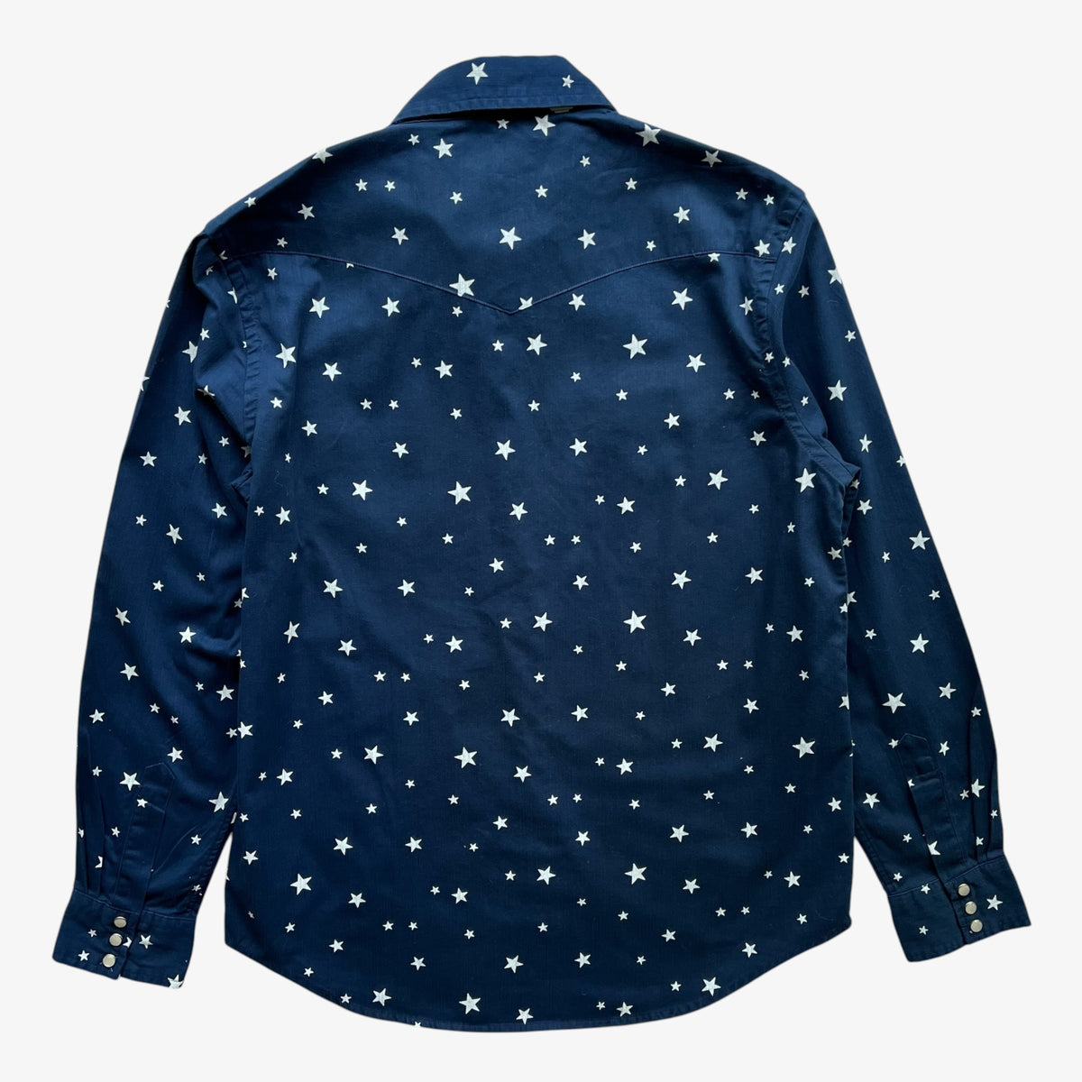 A women's navy blue long-sleeve button-up shirt with an all-over white star pattern, shown from the back on a light grey background.