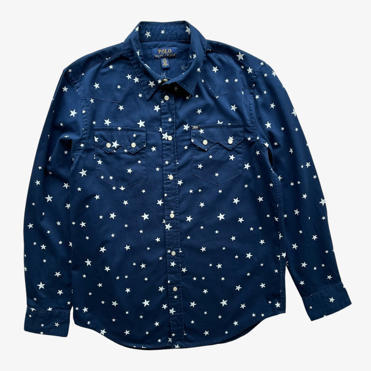 A navy women's long-sleeve button-up shirt with an all-over white star print, featuring two chest pockets and a classic collar, shown flat against a light grey background.