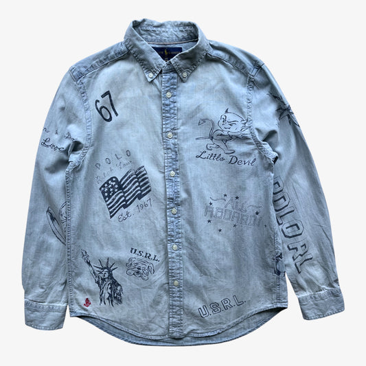A light blue denim women's Ralph Lauren button-up shirt with various graphic prints including an American flag, the Statue of Liberty, 'Little Devil', and '67' on a white background.