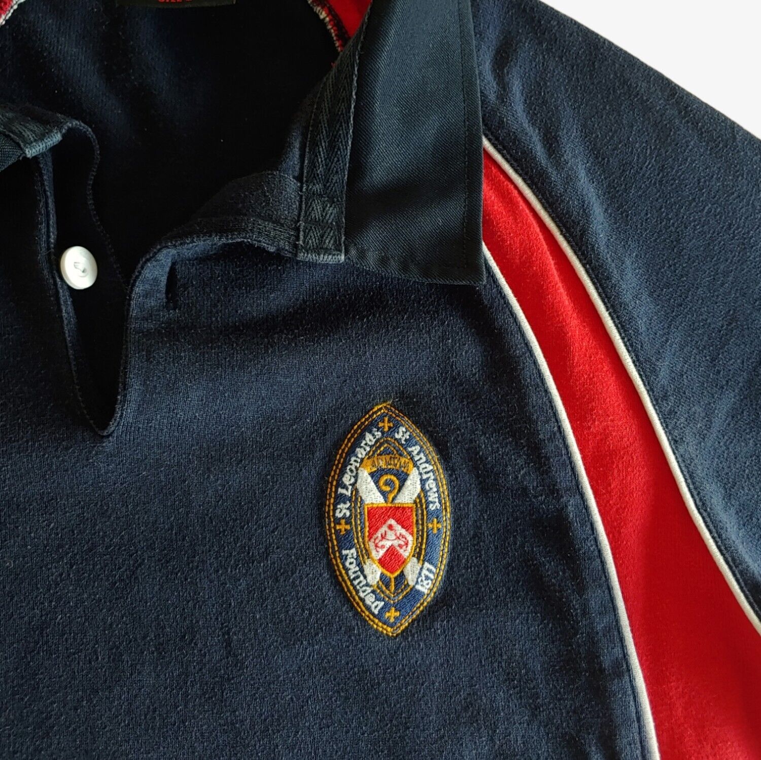 Embroidered St Andrews crest on navy and red Canterbury rugby shirt.