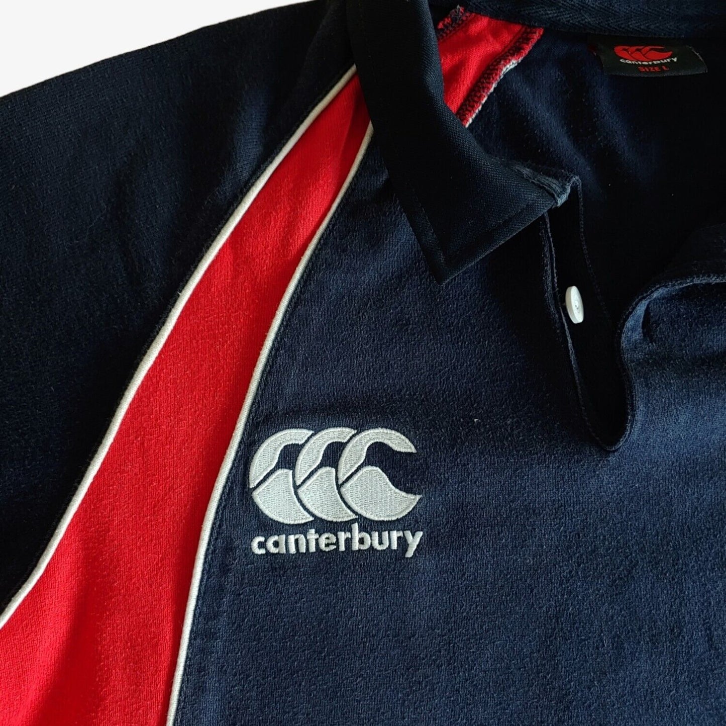 Embroidered Canterbury logo on St Andrews navy rugby shirt.