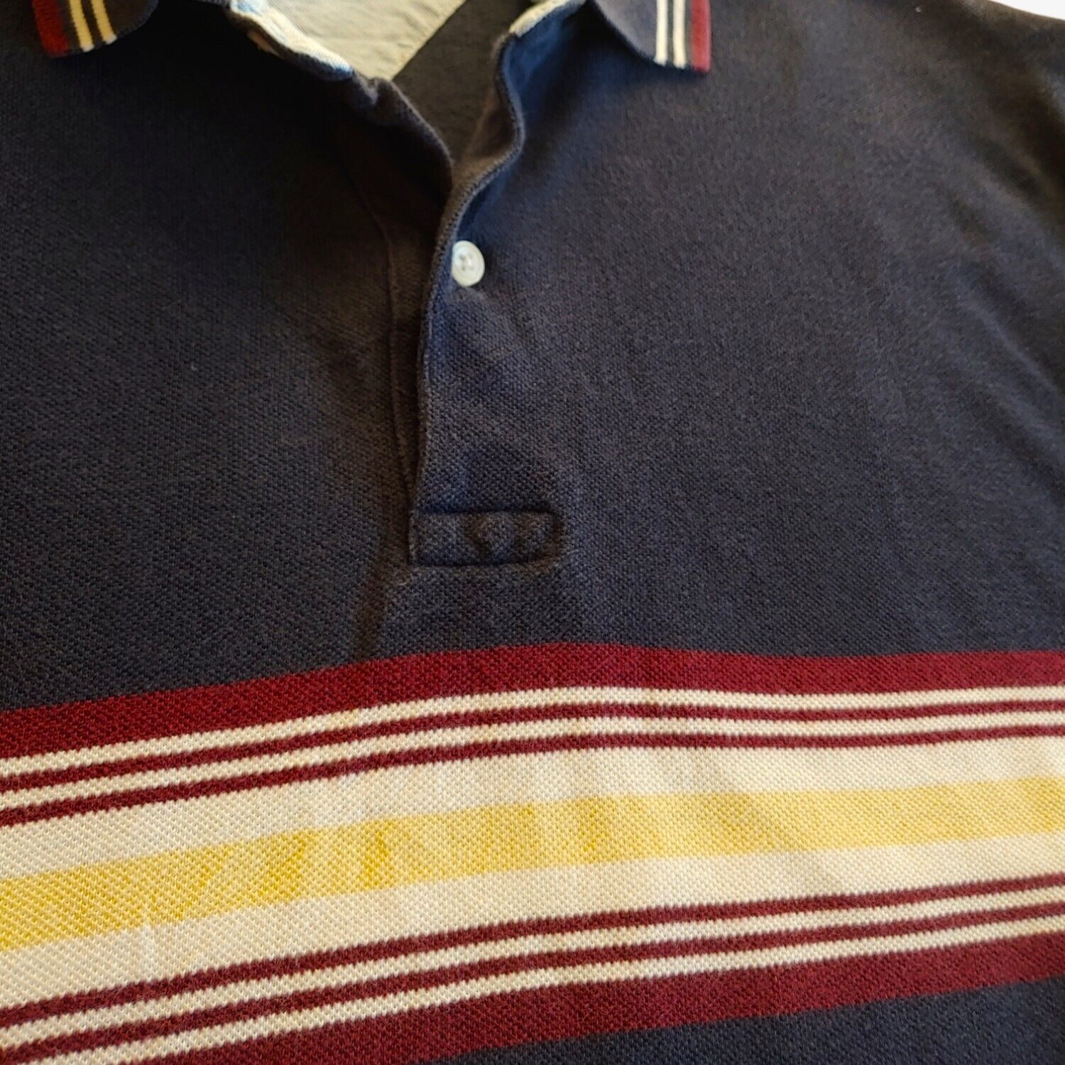 Close up of vintage Tommy Hilfiger striped polo shirt in navy with a colourful stripe.