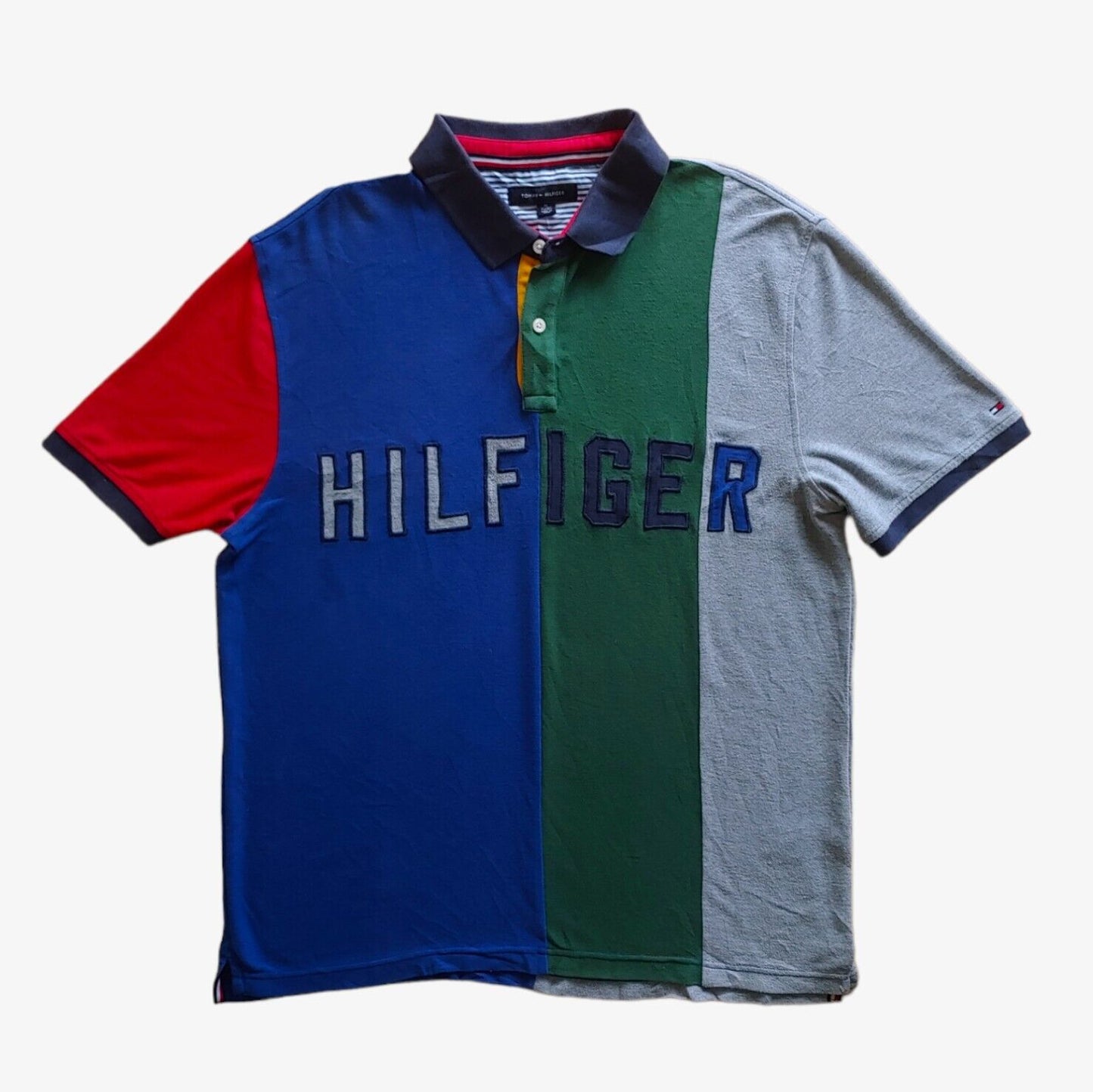 A colour blocked Tommy Hilfiger polo shirt with an embroidered chest logo, featuring a combination of blue, red, green, and grey colours.
